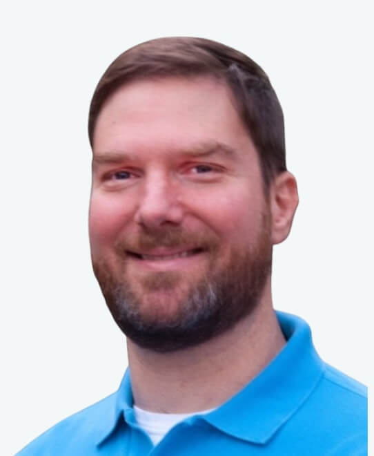 A man with short brown hair and a beard, wearing a light blue collared shirt, smiles at the camera against a plain light background, representing Team V2’s Tech Leads.