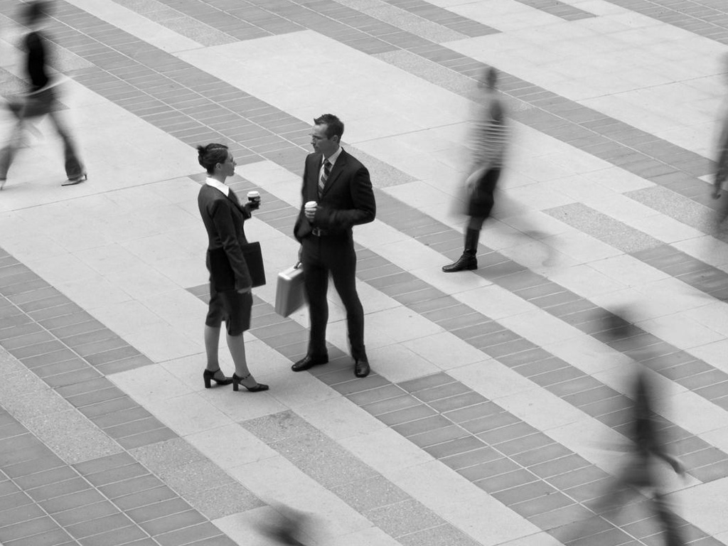 Two in-focus business-people amidst a sea of out of focus people in a black and white photo.