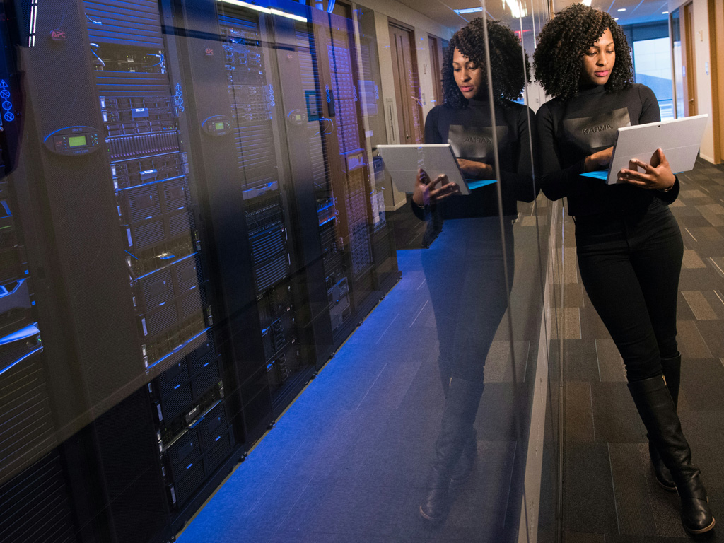 Business woman standing with laptop by a data center computer glass wall image. Photo by Christina @ wocintechchat.com on Unsplash.