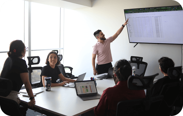 A man stands and points at a large screen displaying a spreadsheet.