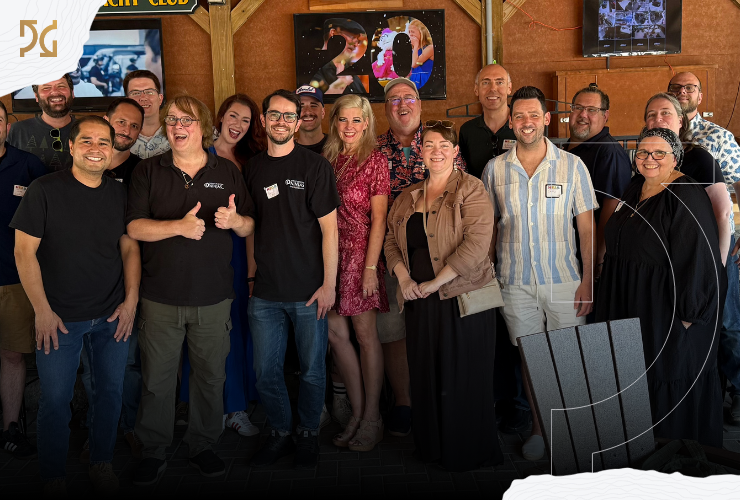 A group of people pose and smile for a photo indoors, some wearing nametags with Internet Marketing Ninjas branding, with TVs and wooden walls in the background.