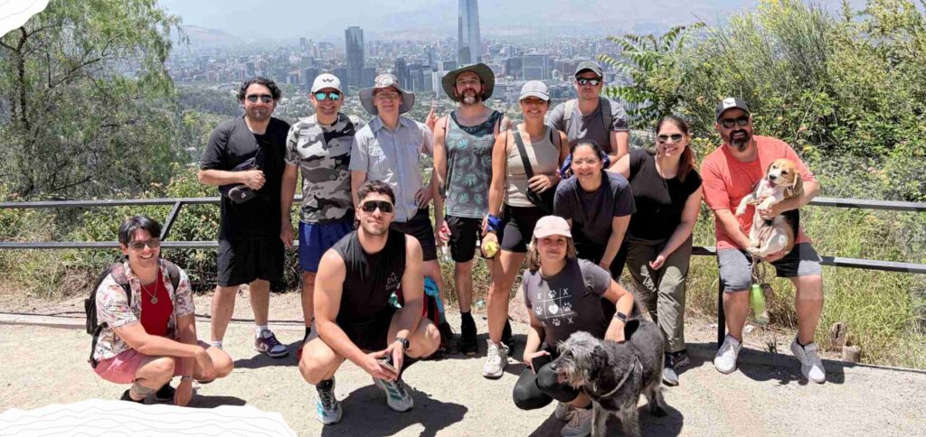 A group of thirteen people and two dogs pose outdoors on a hilltop with a cityscape and mountains in the background, capturing the spirit of teamwork featured in our 2025 Annual Report.
