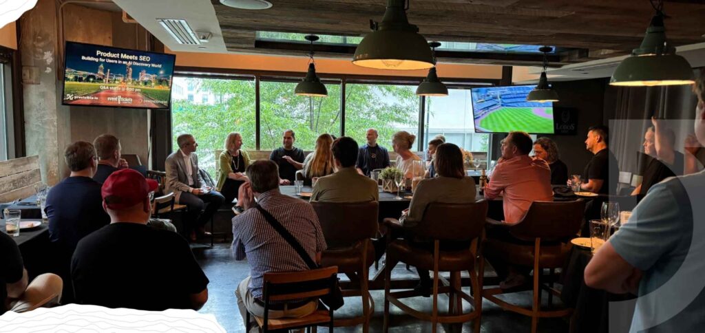 A group of people sit in a dimly lit room, listening to a panel discussion; presentation slides, including highlights from the 2025 Annual Report, are displayed on two screens at the front.