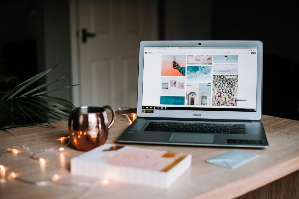 A laptop displaying a photo gallery sits on a wooden desk with a copper mug, closed notebook, string lights, and an envelope nearby—an inviting setup that can enhance brand perception during every website visit.