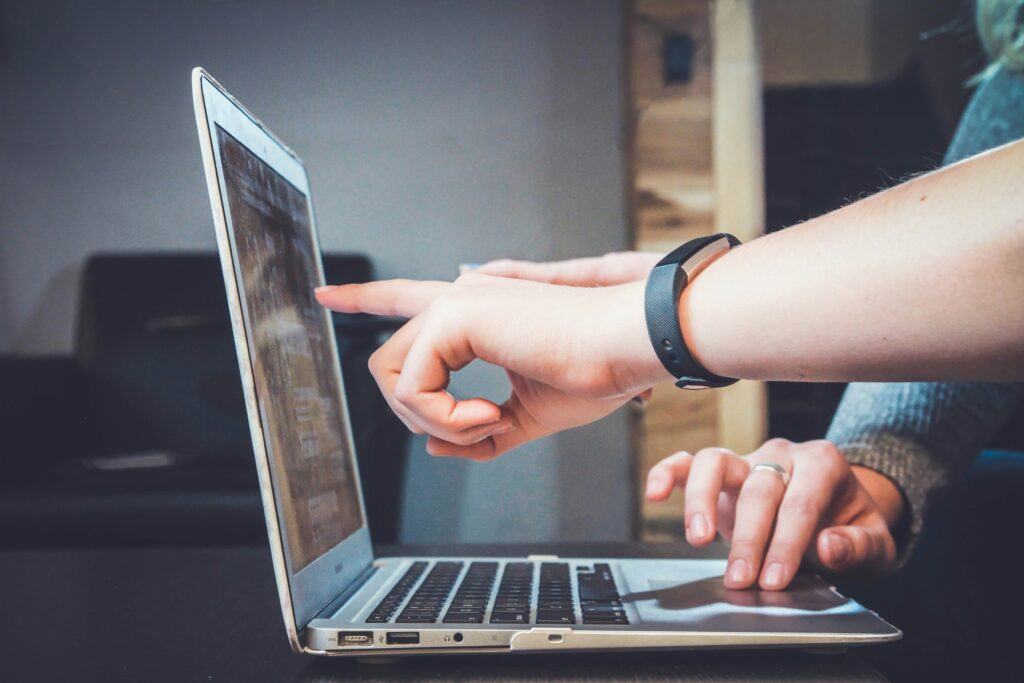 Two people interact with a laptop; one points at the screen—perhaps highlighting website updates or AI visibility insights—while the other types on the keyboard.