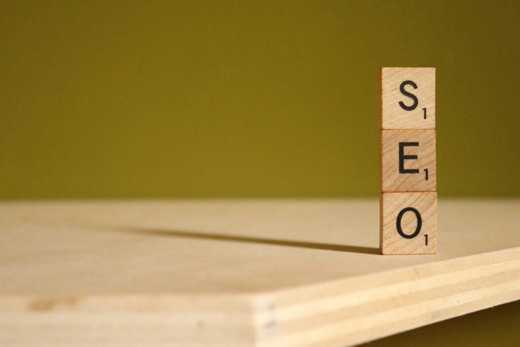 Three wooden Scrabble tiles stacked vertically on a wooden surface spell "SEO" against a plain green background, highlighting SEO fundamentals essential for success in search.