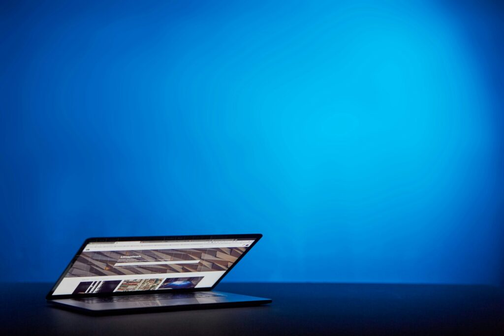 A partially open laptop sits on a dark surface against a plain, bright blue background, ready for buyers to browse site visit reports or explore brand opinions.